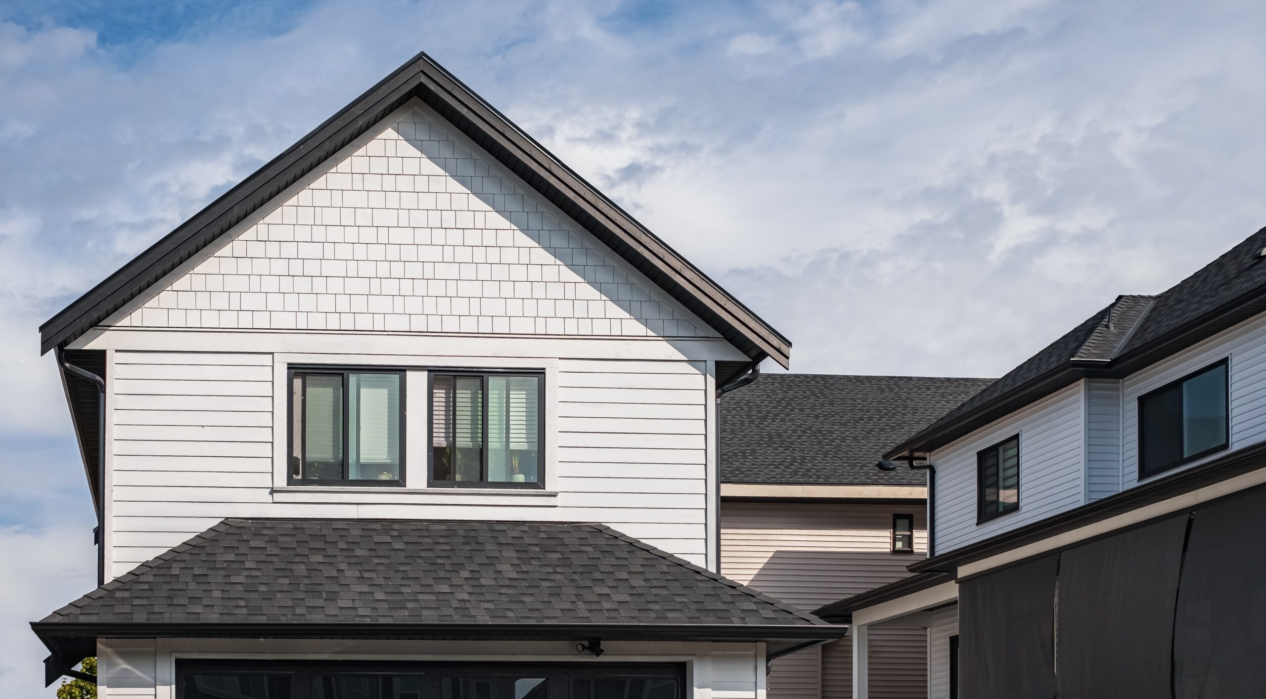 A modern two-story house with white siding, black trim, and dark gray roof shingles under a partly cloudy sky.