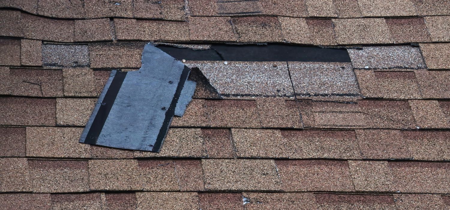 Damaged asphalt roof shingles with lifted flashing, showing a potential leak area requiring repair.