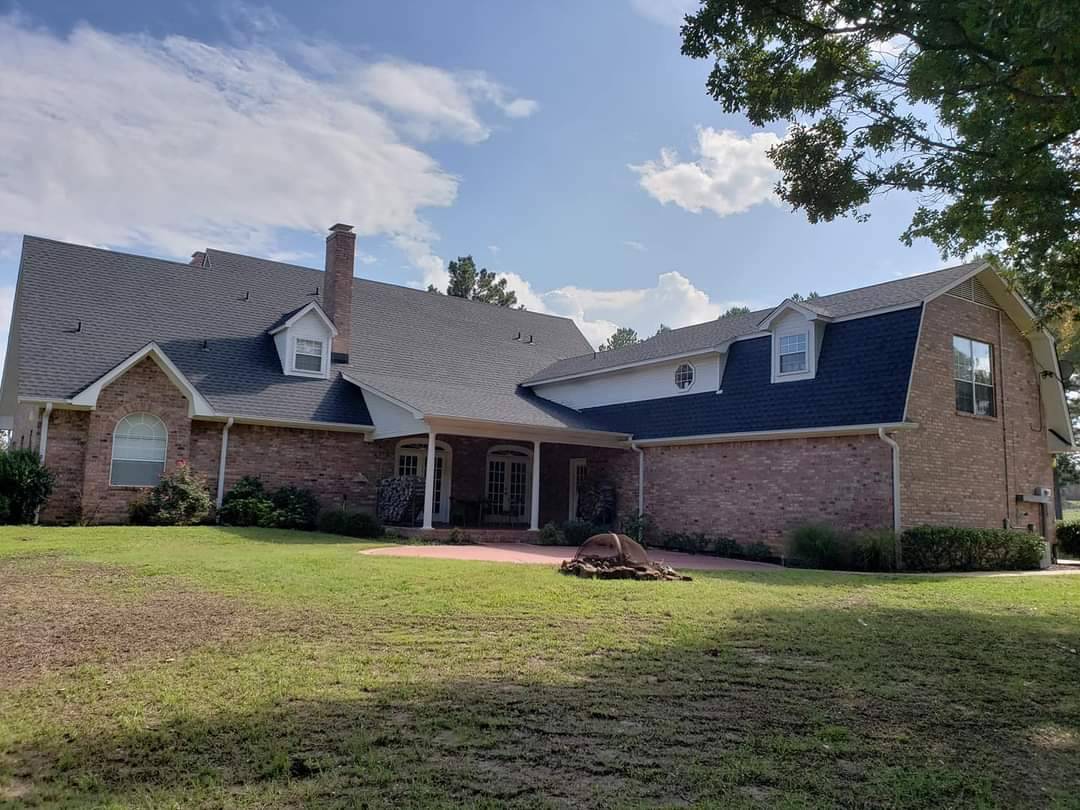 A large two-story brick house with a dark gray roof, front porch, and well-kept lawn under a partly cloudy sky.