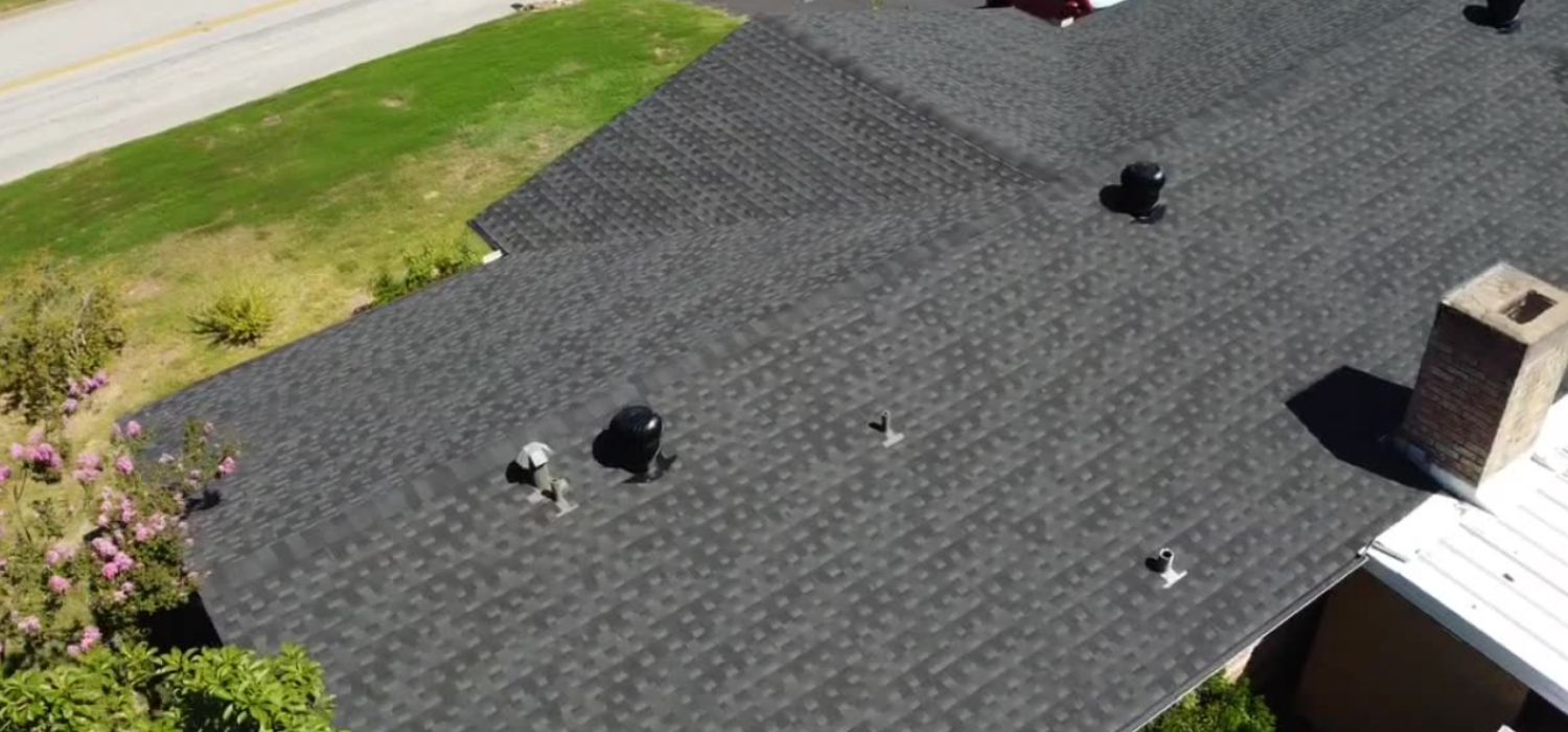 Aerial view of a dark asphalt shingle roof on a residential home with multiple vents and a brick chimney.