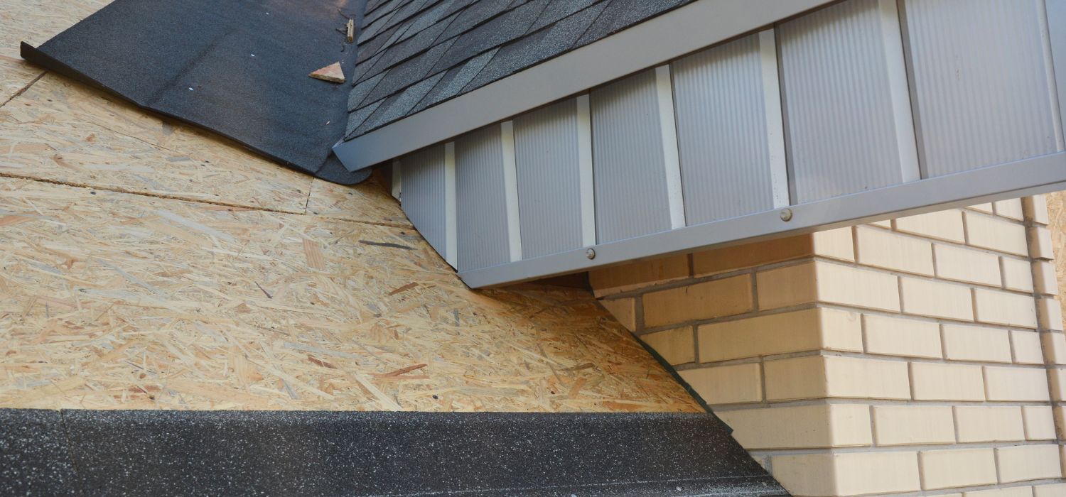Metal roof flashing installed where an asphalt shingle roof meets a brick wall, showing exposed sheathing and flashing that directs water away from the wall and roof joint.